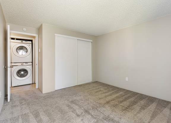 A bedroom with a closet and carpet. Across the hallway from a washer and dryer.
