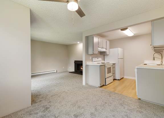 A kitchen area with a white refrigerator, sink, and oven. And grey cabinets.