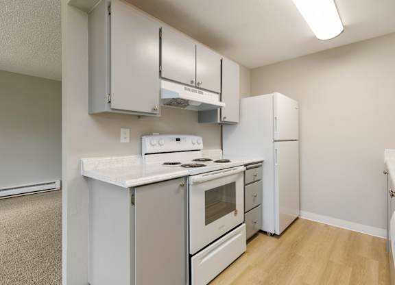 A kitchen with white appliances and  wood plank flooring.