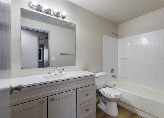 A white bathroom with a sink, mirror, toilet and bathtub.