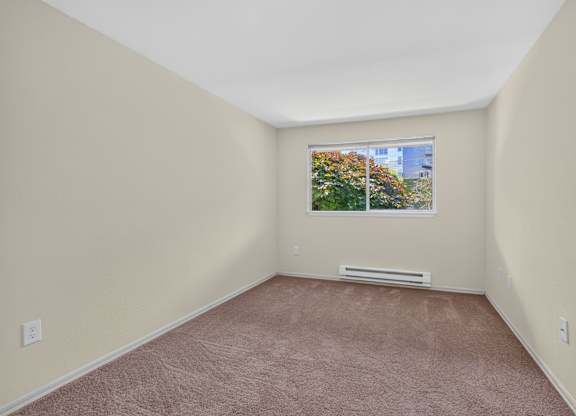 Empty room with a window and a view of trees and buildings outside.