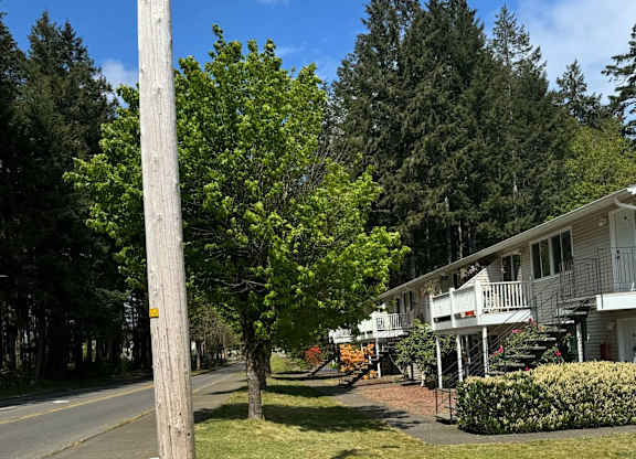 A long wooden pole stands in the grass by a road.