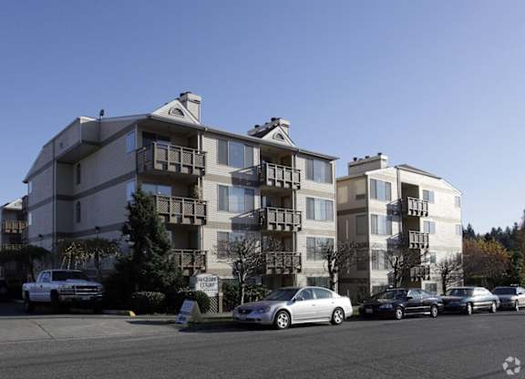 A white car is parked in front of a two-story apartment building.