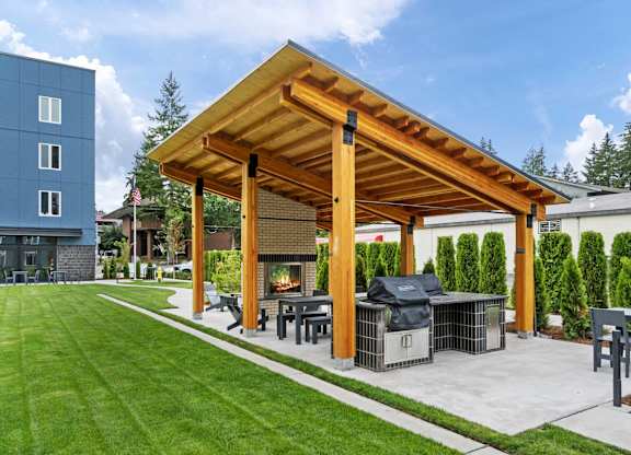 A wooden pergola with a grill and seating area in a backyard at The Hub Apartments, Lacey, WA
