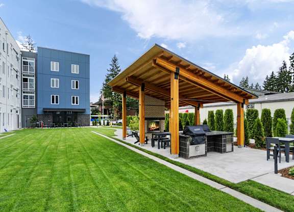 A wooden pavilion is surrounded by a grassy area and a patio with a grill at The Hub Apartments, Lacey, 98503