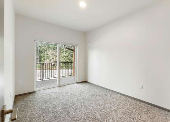A spacious room with a carpeted floor and a sliding glass door leading to a balcony.