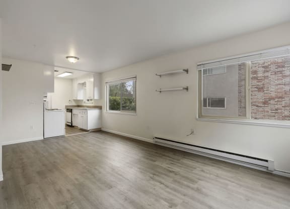 the living room and kitchen of an apartment with wood flooring and a large window