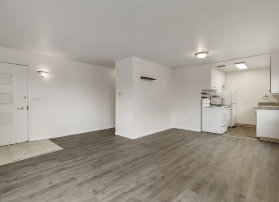 the living room and kitchen of an apartment with white walls and wood flooring