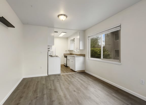 the living room and kitchen of an apartment with white walls and wood flooring