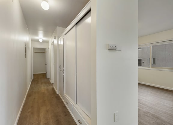 a long hallway with white walls and wood floors and a window