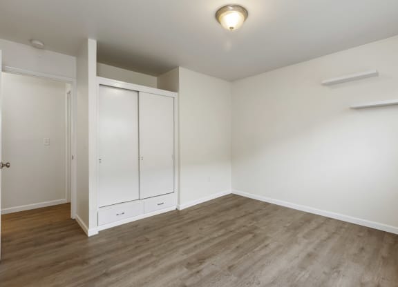 a bedroom with white walls and wood flooring and a closet