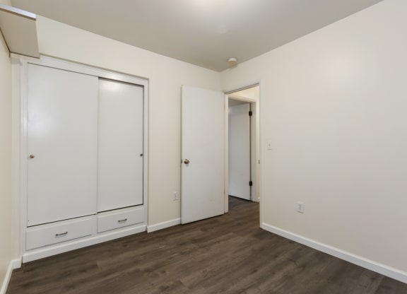 a bedroom with white walls and wood flooring and white closets