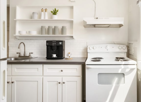 a kitchen with white cabinets and a white stove and a window