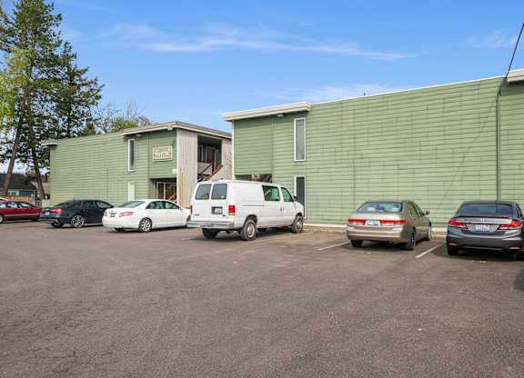 A parking lot with cars and a green building in the background.