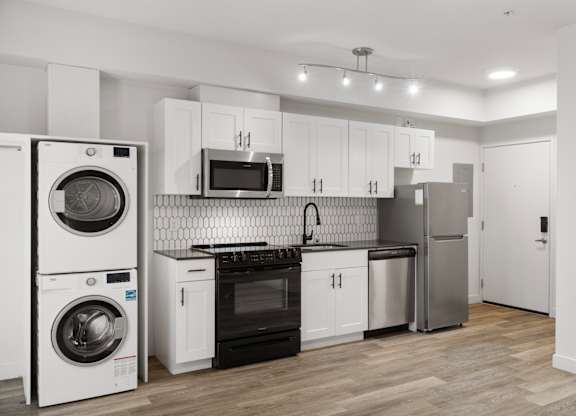 Modern studio apartment at Bode-88 in Seattle with stainless steel appliances, in-home washer and dryer, white shaker cabinets, and tile backsplash