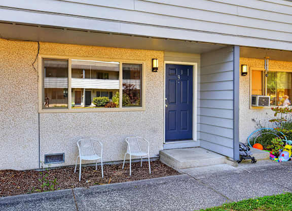 Two white chairs are placed on the concrete in front of a house.
