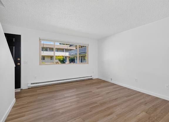 A room with wooden flooring and a large window showing an outdoor view.