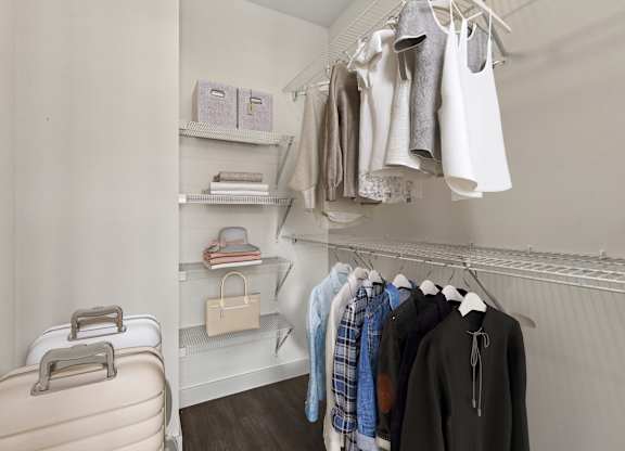 A suitcase is on the floor next to a closet with clothes hanging.