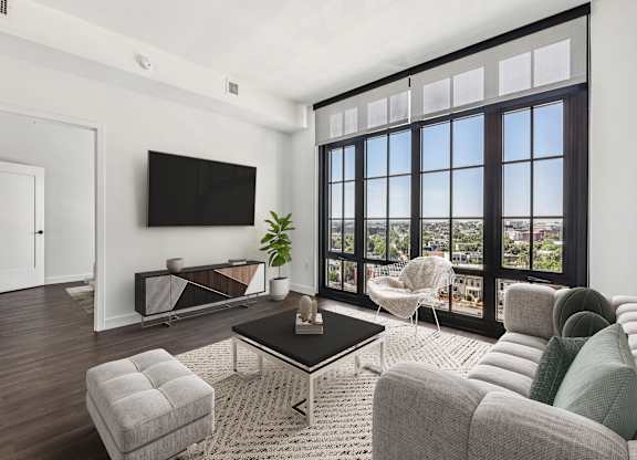 A living room with a flat screen TV mounted on the wall and a large window with a view of the city.