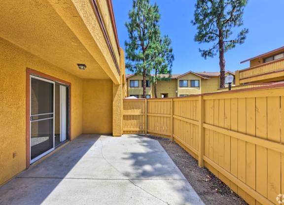 A yellow house with a wooden fence and a tree in the background.