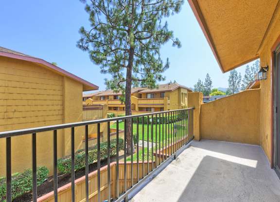 A balcony with a black railing and a tree in the background.