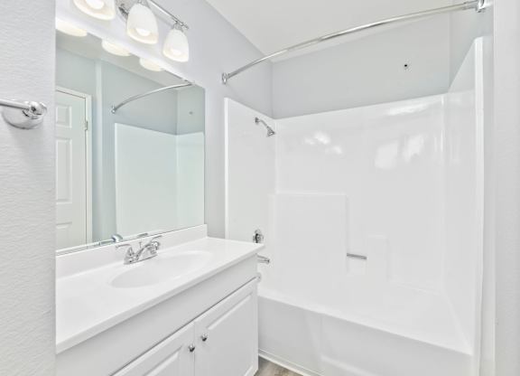 A white bathroom with a sink, mirror, and shower.