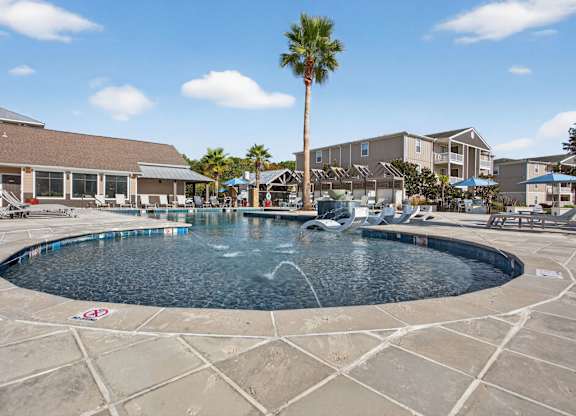 A large swimming pool surrounded by a tiled patio and a palm tree.