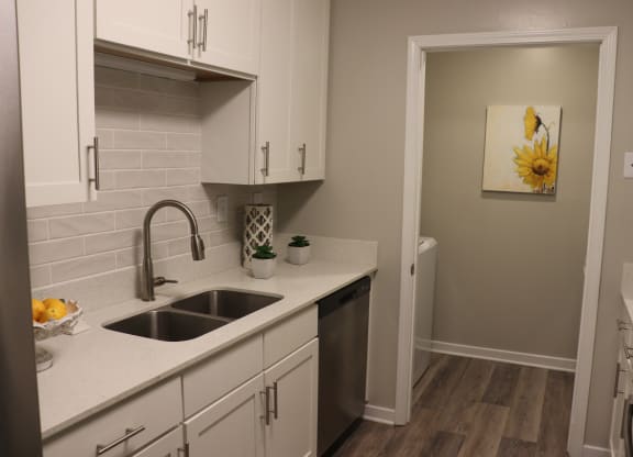 a kitchen with white cabinets and a sink and a door to a bathroom  at Laurelwood Apartment Homes, Laurel, Mississippi