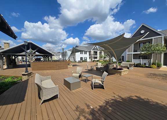 A wooden deck with chairs and tables is surrounded by buildings.