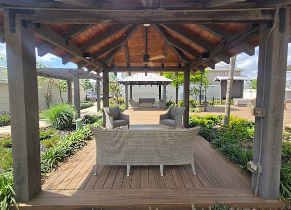 A wooden gazebo with grey cushioned chairs and a table in the middle.