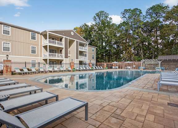 A large swimming pool surrounded by lounge chairs and a building in the background.