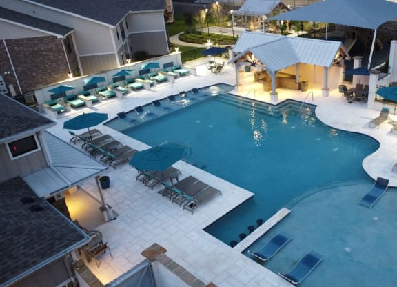 a large swimming pool with lounge chairs and umbrellas at night at Parkwest Apartment Homes, Mississippi