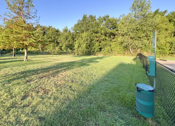 a grassy field with a fence and a trash can at The Madison Apartment Homes in Texas 75703