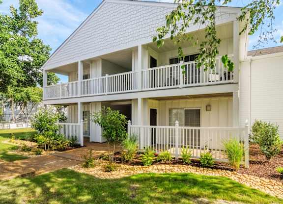 A white two-story house with a balcony and a small garden in front.
