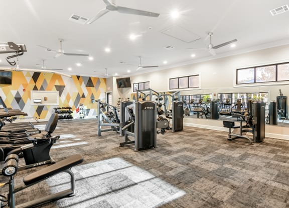 a gym with cardio machines and weights on a carpeted floor at Crossgates Apartment Homes, Starkville, Mississippi