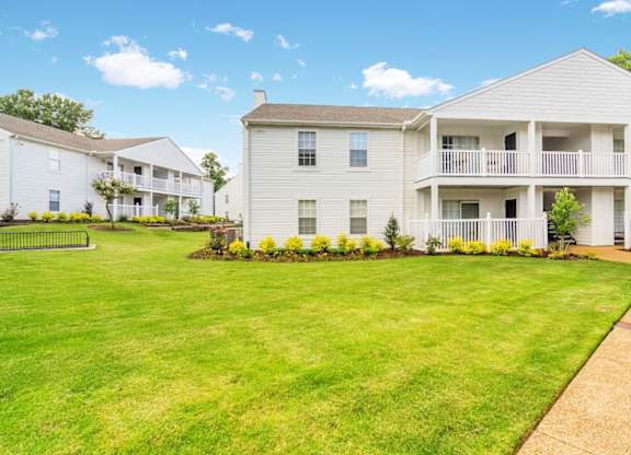A white building with a balcony is surrounded by a green lawn.