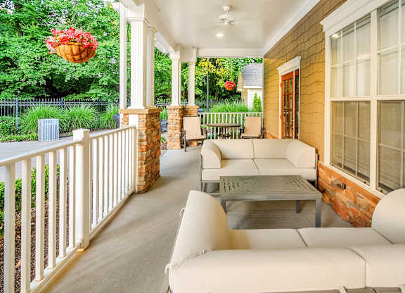 A white sofa and table are on a porch with a red flower hanging from the ceiling.