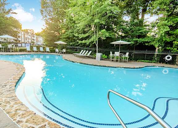 A swimming pool surrounded by trees and chairs.