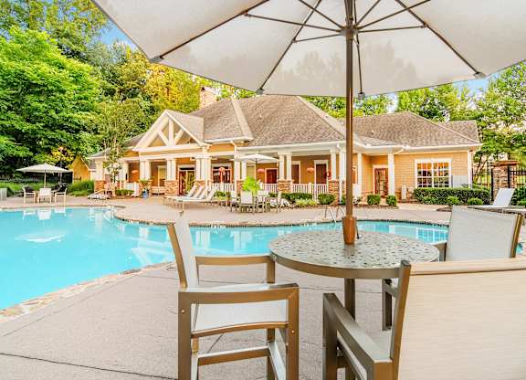 A poolside table with chairs and an umbrella in front of a house.