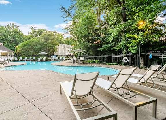 A pool surrounded by trees and chairs.