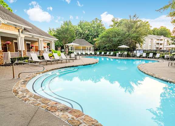 A large swimming pool surrounded by a stone border and lounge chairs.
