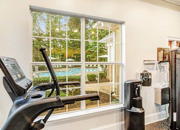 A treadmill is in a room with a window overlooking a pool.