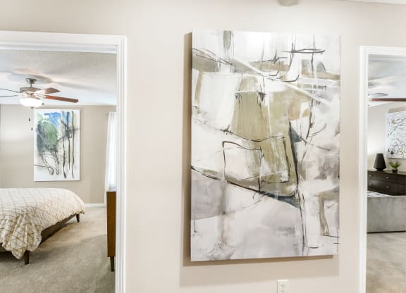 a living room with a painting and a bedroom with a bed at Crossgates Apartment Homes, Starkville, Mississippi