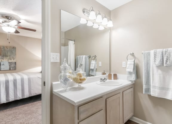 an open bathroom with a sink and mirror and a bedroom with a bed at Avalon Apartments Starkville, MS