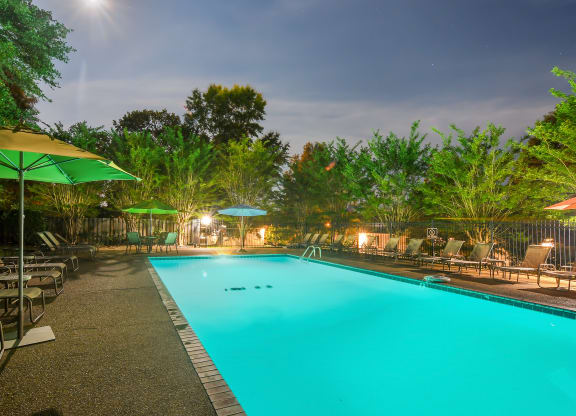 a swimming pool with chairs and umbrellas at night at Parklane Apartment Homes, McComb