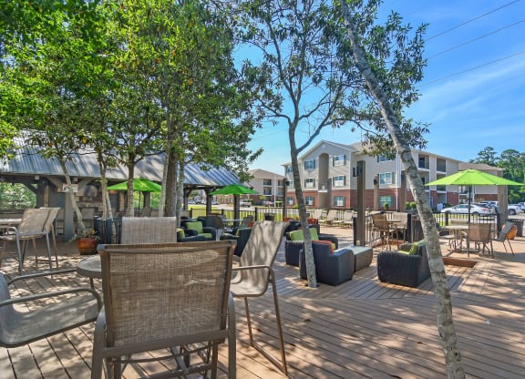 a patio with tables chairs and umbrellas and a building in the background at Lagniappe of Biloxi Apartment Homes, Biloxi, MS