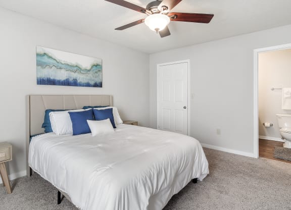 a bedroom with a white bed and a ceiling fan at The Pointe Apartment Homes in Gautier, MS 39553
