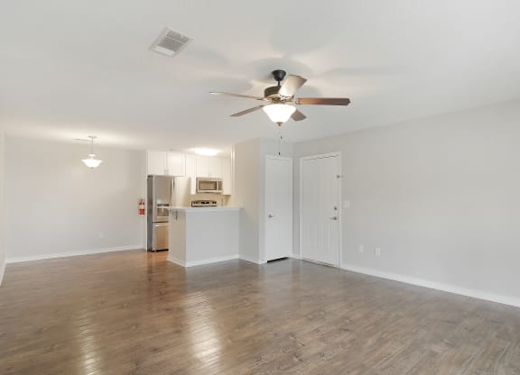 an empty living room with a ceiling fan and a kitchen at The Woodlands Apartment Homes, Meridian, MS