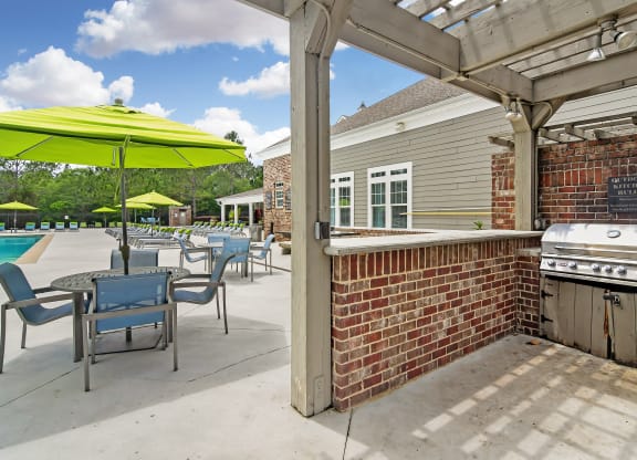 a covered patio with a barbecue grill and tables with umbrellas at Charleston Apartment Homes, Mobile, 36695