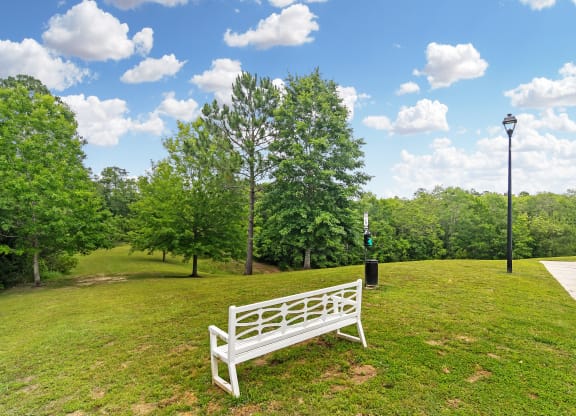 a park bench sitting in the grass next to a sidewalk at Charleston Apartment Homes, Mobile